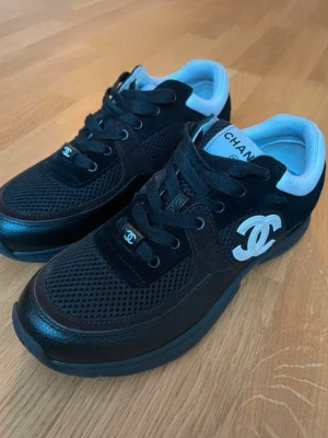 Svarta  sneakers med vit logga - Snygga svarta sneakers med vit CC-logga på sidan och på sulan. Skorna har meshdetaljer, svarta skosnören och vit insida. Perfekta för dig som vill ha en lyxig och trendig look med streetkänsla.