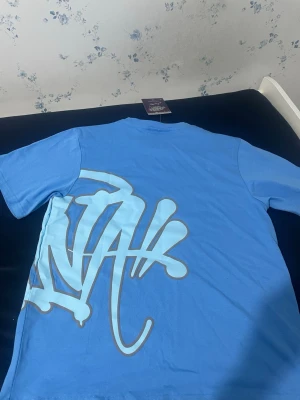 Blått set med graffiti-tryck - Säljer ett blått set med t-shirt och shorts i mjukt material. Båda plaggen har stora graffiti-inspirerade tryck i ljusblått och vitt. Shortsen har resårmidja med vit dragsko. Perfekt för en avslappnad och trendig look.Vi kan komma överens med priset