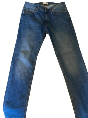 Blå raka jeans från Jack & Jones - Säljer ett par klassiska blå jeans från Jack & Jones med rak passform och fem fickor. Jeansen har snygga slitningar och kontrastsömmar. Tillverkade i bomull med en skön stretch för extra komfort. Perfekta till din vardagsstil!