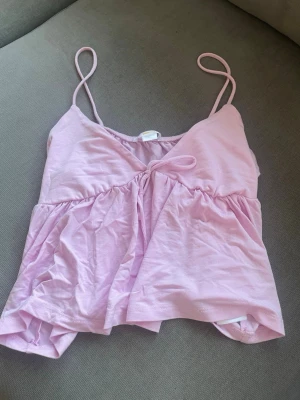 Ljusrosa linnetopp från Gina Tricot - Supersöt ljusrosa linnetopp från Gina Tricot med tunna axelband och v-ringning. Toppen har en liten knytning framtill och är tillverkad i mjuk bomull. Perfekt för varma dagar och enkel att styla med jeans eller kjol. Säljer så den aldrig kommit till användning 💕💕