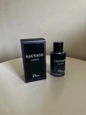 Dior Sauvage Eau de Parfum 60ml - Dior Sauvage Eau de Parfum med elegant svart glasflaska och matchande svart kartong. Flaskan har en stilren, rund form och tydlig logga framtill. Doften är känd för sin fräscha och maskulina karaktär, perfekt för dig som vill sticka ut. Ca 60% av parfymen kvar!