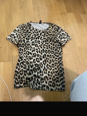 Leopardmönstrad t-shirt från H&M - Säljer en snygg leopardmönstrad t-shirt från H&M Divided. T-shirten har korta ärmar och rund halsringning. Materialet är mjukt och skönt, perfekt för dig som vill sticka ut lite extra. Passar till allt.