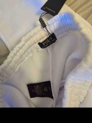 Vita mjukisbyxor från Polo Ralph Lauren - Snygga vita mjukisbyxor från Polo Ralph Lauren med resår i midjan och mjukt, fleeceliknande material på insidan. Perfekta för en avslappnad stil och riktigt sköna att ha på sig. Klassisk design med raka ben och diskret logga på etiketten.