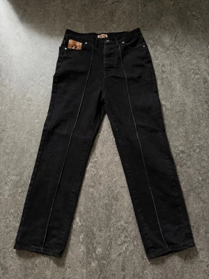 Svarta corteiz jeans - Tja, säljer ett par svarta korta jeansmed raka ben och kontrastsömmar. På bakfickorna finns broderade motiv, inklusive det kallblodiga corteiz märket. Jeansen har klassisk femficksdesign och är tillverkade i denim. Perfekta för dig som vill sticka ut med coola detaljer och tycker om kläder av något extra! Vid funderingar så är det bara att skriva.