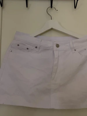 Vit kortkjol med fickor - Snygg vit kortkjol med klassisk femficksdesign och knappstängning fram. Kjolen har bälteshällor och är perfekt för en fräsch och enkel stil. Passar till många olika outfits och är lätt att matcha.