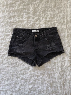 Snygga svarta slitna jeansshorts - Supercoola svarta jeansshorts i en snygg urtvättad nyans. Shortsen har rejäla slitna detaljer fram, råa fransade benslut och lätt slitna detaljer på bakfickorna. Klassisk 5-fickorsmodell som är perfekt till sommaren. Storlek 38 (alla mått finns i bilderna). Skickar snabbt!!💗