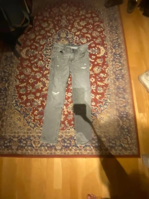 Ljusgrå slim fit jeans med slitningar - Säljer ett par ljusgrå slim fit  jeans med slitna detaljer på framsidan. Jeansen har klassisk femficksdesign och normal midja. Perfekta för en avslappnad och trendig look.