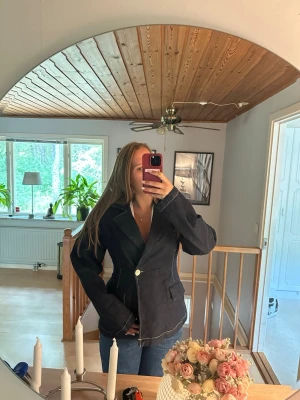 Mörkblå figursydd jeanskavaj - Snygg mörkblå jeanskavaj med kontrastsömmar. Kavajen har två framfickor och stängs med en knapp framtill. Perfekt för en avslappnad men ändå stilren look. Materialet är denim och modellen är figursydd. Använd en gång. Passar även M. 