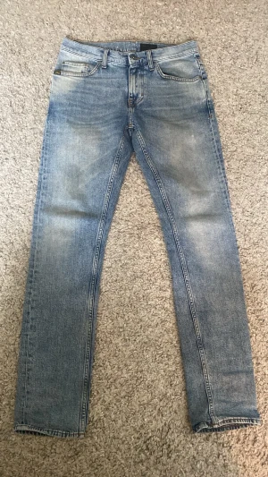 Ljusblå raka/slim fit jeans från Tiger of sweden - Säljer ett par ljusblå jeans med raka ben och klassisk femficksmodell. Jeansen har en snygg tvätt med slitningar och är tillverkade i denim. Passar perfekt till en avslappnad stil och är riktigt bekväma. Storlek W29 L32. Priset är inte hugget i sten 😊