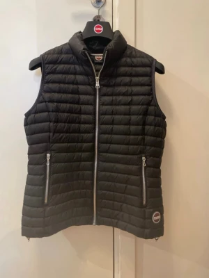 Svart dunväst från Colmar - Snygg svart dunväst från Colmar med quiltad design och två dragkedjeförsedda fickor framtill. Västen har hög krage och diskret logga på nedre vänstra sidan. Perfekt för lager-på-lager och håller dig varm under kyliga dagar.