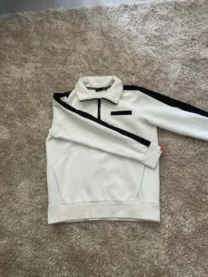 Sail racing halvzip - Snygg vit tröja med halv dragkedja och svarta ränder längs ärmarna. Tröjan har hög krage och fickor framtill. Perfekt för en sportig och stilren look. Materialet känns mjukt och bekvämt.