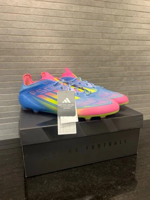 Adidas F50 Elite AG - Säljer ett par Adidas F50 fotbollsskor i en riktigt färgstark design med blå, rosa och gula detaljer. Skorna har låg profil, snörning och är tillverkade i syntetmaterial för bästa känsla på planen. Perfekta för dig som vill sticka ut och ha grym kontroll på konstgräs.