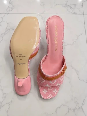 Rosa Louis Vuitton pumps med monogram - Säljer ett par rosa pumps från Louis Vuitton med klassiskt monogrammönster i vitt. Skorna har öppen tå, smal klack och en brun läderdetalj med guldfärgad LV-logga framtill. Materialet är tyg och läder, och innersulan är rosa med Louis Vuitton-tryck.