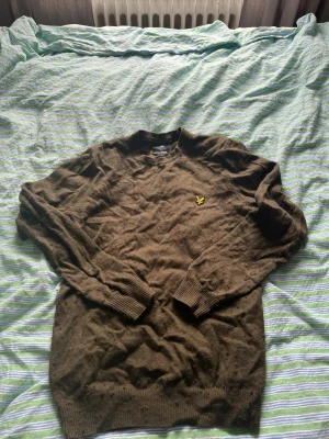 Brun stickad tröja från Lyle & Scott - Snygg brun stickad tröja från Lyle & Scott med rund halsringning och klassisk gul logga på bröstet. Tröjan har långa ärmar och ribbade muddar vid ärmslut och nederkant. Tyget är lite frissigt därför priset går att pruta ner!