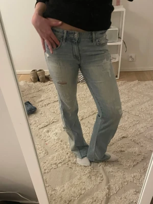 Ljusblå raka jeans med slitningar - Säljer ett par ljusblå jeans med raka ben och snygga slitningar på både fram- och baksida. Jeansen har klassisk femficksmodell och normal midja. Perfekta för en avslappnad och trendig look. Väldigt efterfrågade 