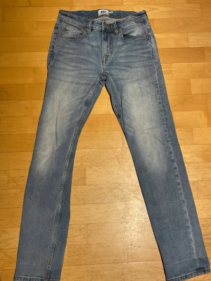 Ljusblå raka jeans - Säljer ett par ljusblå jeans med raka ben och klassisk femficksmodell. Jeansen har snygga slitningar och en något tvättad look. Perfekta för dig som gillar en avslappnad och trendig stil.