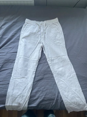 Beige byxor  - Säljer ett par beige byxor med avslappnad passform och dragsko i midjan. Byxorna har sidofickor fram och två fickor bak. Perfekta för en chill och luftig stil under varma dagar.