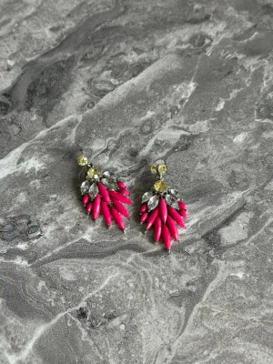 Färgglada örhängen med rosa detaljer - Snygga örhängen med klara rosa pärlliknande detaljer och gnistrande stenar i silver och ljusgul färg. Örhängena har en unik form med spetsiga pärlor och glittriga inslag som verkligen drar blickarna till sig. Perfekta för dig som vill sticka ut med accessoarerna.