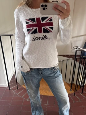 Vit stickad tröja från Morris - Vit stickad tröja i rött, svart och vitt. Tröjan har rund halsringning, långa ärmar och en liten broderad detalj vid ärmslutet. Perfekt för dig som gillar coola statement-plagg.