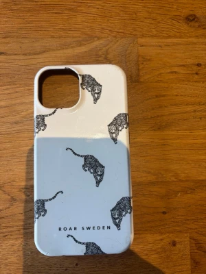 Vitt mobilskal med leopardmönster - Snyggt vitt mobilskal från ROAR SWEDEN med svarta leopardhuvuden som mönster. Skalet har en stilren design och är gjort i hårdplast som skyddar mobilen. Passar perfekt för dig som vill ha ett unikt och trendigt skal.