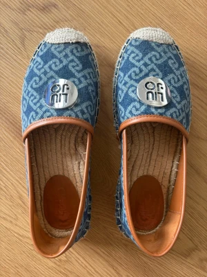 Blå denim loafers från Liu Jo - Snygga loafers i blå denim med ljusbrunt läder runt öppningen och grovsydd sula i repstil. Skorna har ett mönster i tyget och en stor silverfärgad Liu Jo-logga framtill. Perfekta för dig som gillar en avslappnad men trendig look.