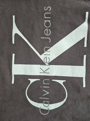Brun sweatshirt från Calvin Klein Jeans - Snygg brun sweatshirt från Calvin Klein Jeans med stort vitt logotryck på framsidan. Tröjan har rund halsringning och är tillverkad i mjukt material som passar perfekt till en avslappnad stil.