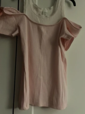 Ljusrosa ribbad offshoulder topp - Söt ljusrosa topp med ribbad struktur och offshoulder-design. Toppen har korta ärmar och en mjuk, stretchig passform som ger en avslappnad men ändå trendig look. Perfekt för dig som gillar en feminin och enkel stil.