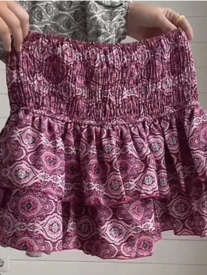 Rosa mönstrad volangkjol - Supersöt kort kjol i rosa med vitt och lila mönster. Kjolen har bred smock i midjan och dubbla volanger för en extra fluffig look. Perfekt för dig som gillar färg och mönster!