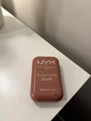 NYX buttermelt blush i varm ton - NYX Professional Makeup buttermelt blush i en varm, brunrosa nyans. Kommer i en smidig, rektangulär dosa med spegel. Perfekt för att ge kinderna en naturlig glow och mjuk finish. Innehåller 5 g produkt.