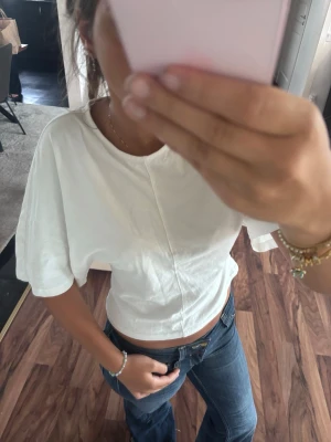 Vit croppad topp med vida ärmar - Säljer en vit croppad topp med vida, korta ärmar och rund hals. Toppen har en enkel och clean design med en lätt struktur i tyget. Perfekt att styla med jeans eller kjol för en trendig look.