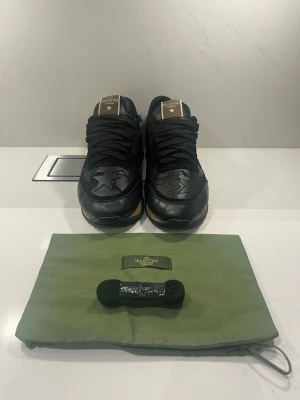 Valentino Rockrunner svarta sneakers - Svarta Valentino Rockrunner sneakers med stjärnmönster i skinn och detaljer i guld på plösen. Snygga nitar i stjärnform på hälen och grov gummisula i svart och beige. Medföljer extra svarta skosnören och grön dustbag med Valentino-logga. Bra kvalitet!