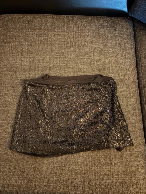 Svart glitter minikjol - Snygg svart minikjol täckt med glittrande paljetter. Kjolen har en rak passform och är perfekt för dig som vill sticka ut. Passar S/M lågmidjad 
