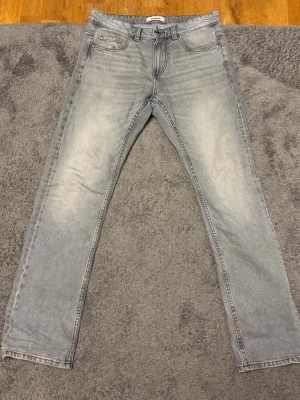 Ljusgrå raka jeans - Snygga ljusgrå jeans med raka ben och klassisk femficksdesign. Jeansen har en lätt tvättad look med slitningar på låren och baksidan. Perfekta för en avslappnad och trendig stil. Materialet är denim i bomull.