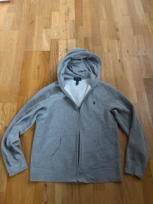 Grå hoodie med dragkedja från Polo Ralph Lauren - Snygg grå hoodie från Polo Ralph Lauren med dragkedja framtill och två fickor. Sällan använt den och är i bra skick. 