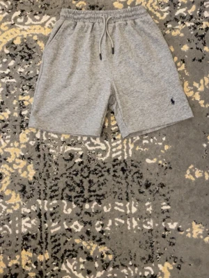 Gråa ralph Laurent  shorts  - Snygga grå shorts i mjukt material med elastisk midja och snörning. Klassisk design med två sidofickor och en liten broderad logga framtill. Perfekta för chill dagar eller träning.
