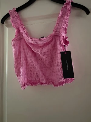 Rosa linne  från Vero Moda - Supersöt rosa linne  topp från Vero Moda med smockat tyg och volangdetaljer på axelbanden. 