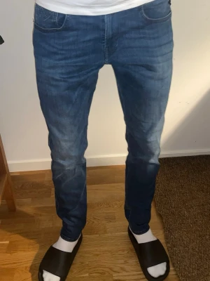 Blåa Repaly Anbass - Snygga blå jeans med raka ben och diskreta slitningar på låren och knäna. Klassisk femficksmodell med knapp- och dragkedjegylf. Jeansen har en något tvättad look och är tillverkade i denim, perfekt för en avslappnad stil.