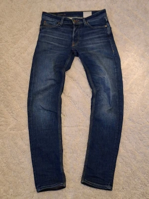 Mörkblå jack & jones slim fit jeans - Snygga mörkblå slim fit jeans med klassisk femficksdesign och lätt slitna detaljer. Jeansen har normal midja och raka ben, perfekta till en avslappnad stil. Tillverkade i stretchigt denimtyg för extra komfort. Står w28 men sitter som w30