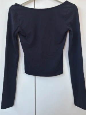 Svart långärmad topp Gina Tricot med lite open back - En svart långärmad topp från Gina Tricot med enkel och stilren design. Toppen har en bred, något båtformad ringning bak och är figurnära i modellen. Perfekt att matcha med jeans eller kjol för en clean look.