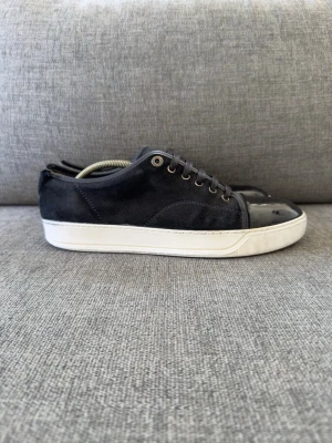 Lanvin cap toe suede/patent sneckers. Uk 8 passar 42-43 - Säljer nu dessa riktigt schyssta skor från lanvin Paris. Model namn - lanvin DBB1 cap toe. Nypriset  på dessa är 5000kr och de är självklart äkta. Skicket är riktigt bra med små defekter som att läderet på båda skor har lossnat där bak vid hälen. Kolla bild 6 för att se en annan liten defekt. Sulkräm har andvänts 
