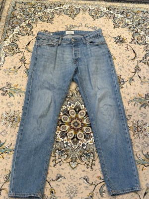 Ljusblå raka jeans - Säljer ett par ljusblå jeans från Jack and Jones med tapered/mike  passform och klassisk femficksdesign. Jeansen har normal midja, gylf med knappar samt detaljerade sömmar. Perfekta för en avslappnad och trendig look. 30/30 men passar nog dig som är 31/30