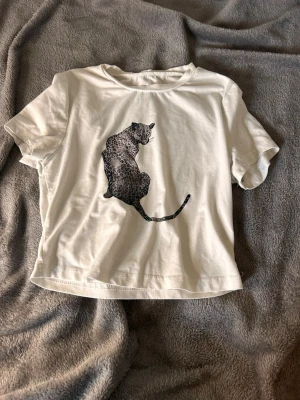 Vit t-shirt med leopardtryck - Säljer en vit t-shirt med ett stort leopardtryck på framsidan. T-shirten har korta ärmar, rund halsringning och är gjord i mjuk bomull. Perfekt för dig som gillar djurmotiv och vill ha en enkel men snygg look.