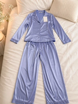 Ny Intimissimi Ljuslila 100% silkpyjamas   - Snygg ljuslila pyjamas i glansigt silk material med prislapp. Setet består av en långärmad skjorta med knappar och krage samt matchande vida byxor med resår i midjan. Perfekt för mysiga kvällar hemma och ger en lyxig känsla. 