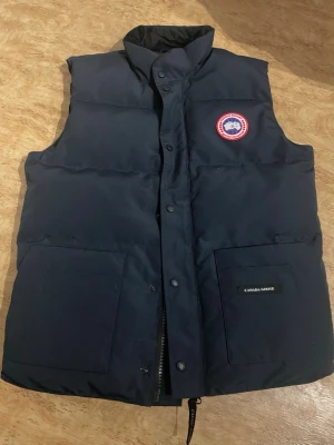 Mörkblå dunväst från Canada Goose - Säljer min Canada Goose i mörkblå färg, storlek M. Jackan/västen är i nyskick och väldigt sparsamt använd utan några defekter.  * Storlek: M * Färg: Mörkblå * Skick: Nyskick * Alla detaljer och märken finns kvar  Köpt som äkta och allt ser korrekt ut efter egen kontroll.  Pris: 999 kr eller vid bra bud. Kan skickas eller mötas upp i Göteborg.Först till kvarn vill ba bli av med den 