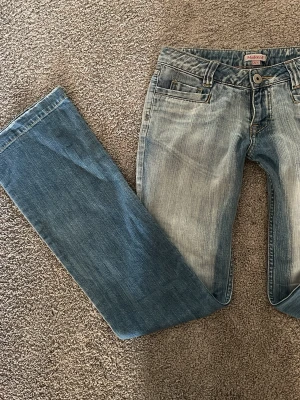 Ljusblå bootcut jeans med slitningar - Säljer ett par ljusblå bootcut jeans med snygga slitningar och tvättade detaljer. Klassisk femficksmodell med bälteshällor och knappgylf. Jeansen har en relaxed passform och är tillverkade i bomull för skön känsla. Börjar på 600kr men det är diskuterbart💞