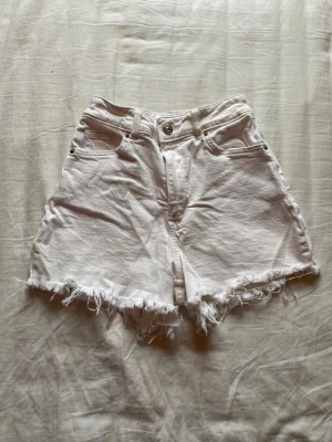 Vita högmidjade jeansshorts med fransar - Snygga vita jeansshorts med hög midja och fransig, rå kant nertill. Klassisk femficksmodell med knapp och dragkedja framtill.