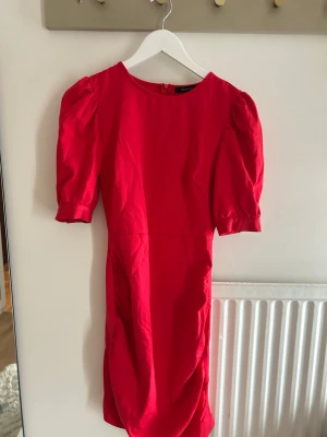 Röd puffärmad kortklänning - Snygg röd kortklänning med puffärmar och rund halsringning. Klänningen har en figurnära passform och dragkedja i ryggen. Perfekt för dig som vill sticka ut med en färgstark look. Sitter jättte smickrande 