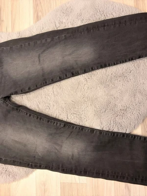 Grå slim fit jeans Dressmann  - Snygga grå slim fit jeans från Dressmann i storlek W30 L32. Jeansen har en tvättad look med ljusare partier och klassisk femficksmodell. Perfekta för dig som gillar en smalare passform och vill ha ett par stilrena jeans till vardagslooken.