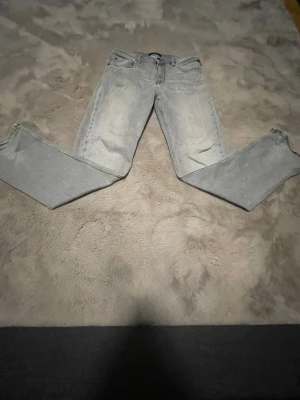 Ljusgrå raka jeans - Säljer ett par ljusgrå jeans med rak passform och klassisk femficksdesign. Jeansen har en tvättad look och detaljerade sömmar på bakfickorna. Perfekta för en avslappnad stil och passar till det mesta i garderoben.