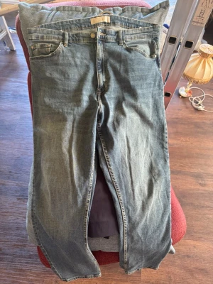 Blå raka jeans med fem fickor - Klassiska blå jeans med rak passform och fem fickor. Jeansen har normal midja, bälteshällor och knappgylf. Materialet är denim i bomull och färgen är en tvättad blå nyans med lätt slitning. Perfekta för en avslappnad och tidlös stil.